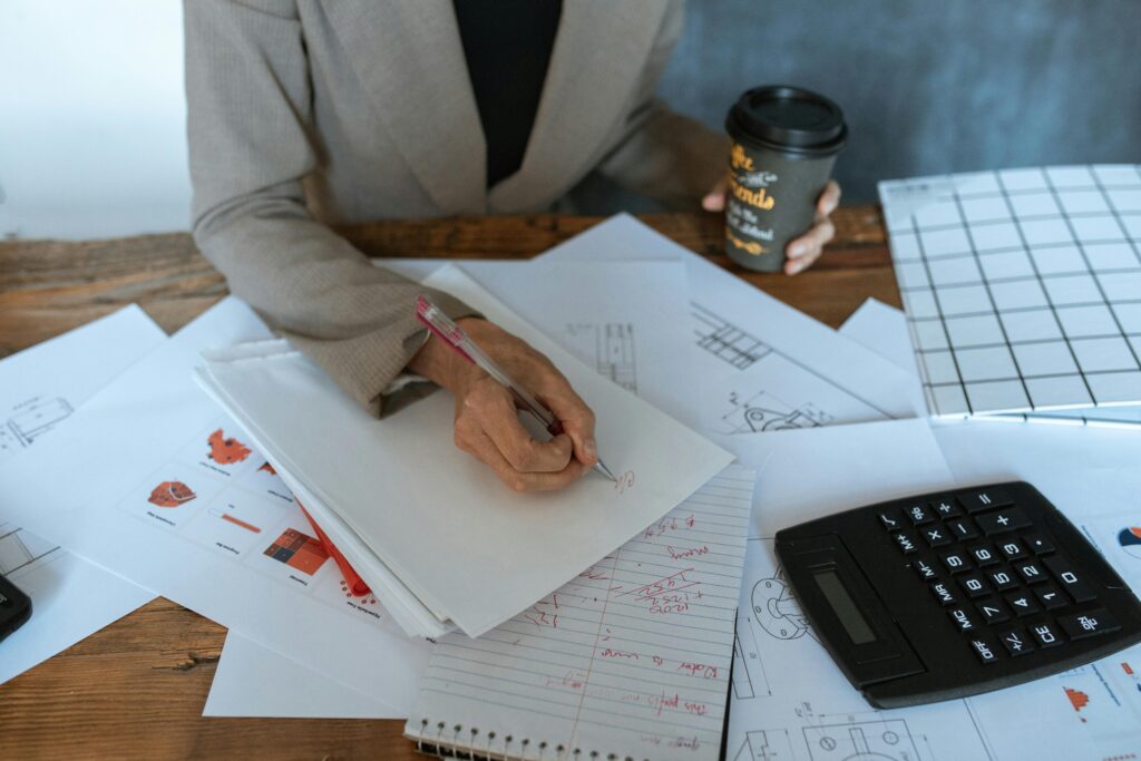 Close-up of a person writing at an office desk with documents and coffee, symbolizing productivity.