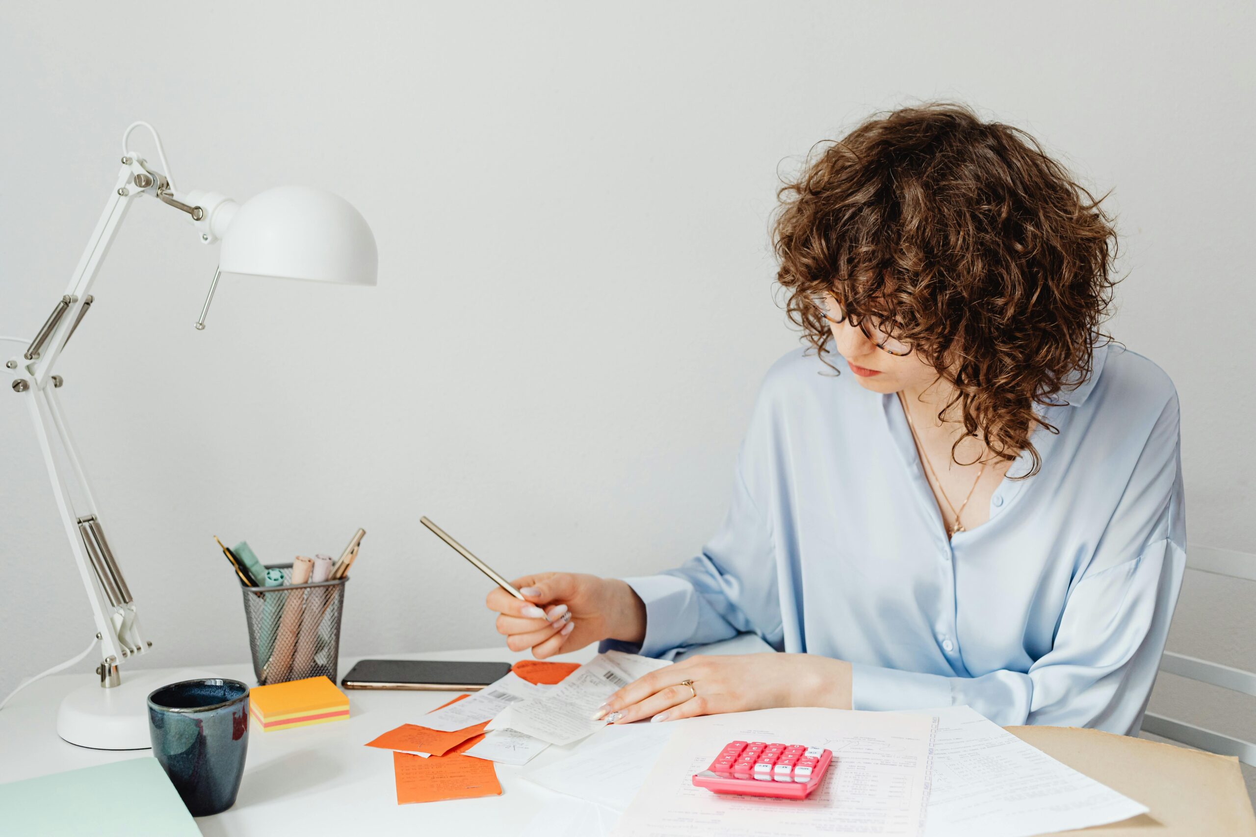 Woman in office calculating expenses with documents, calculator, and coffee.