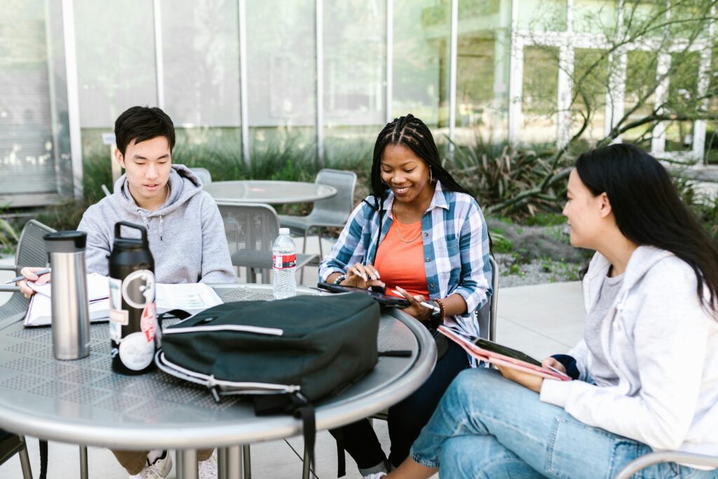 A group of diverse university students studying together outdoors, collaborating with books and tablets.