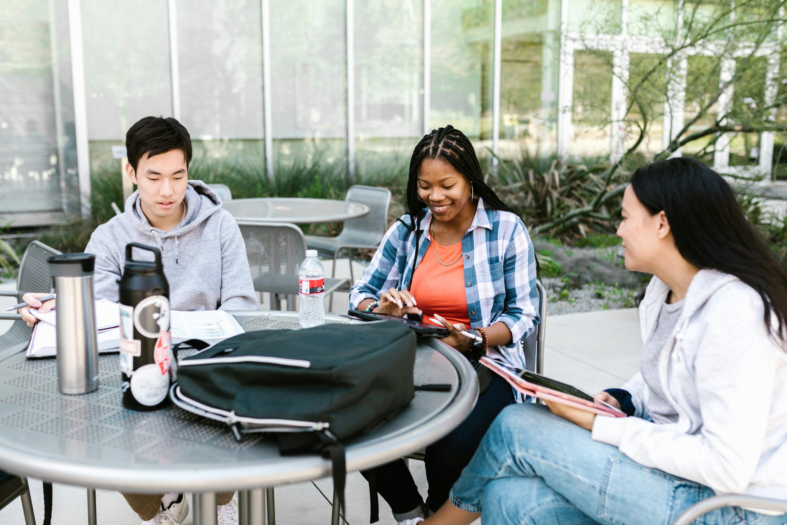 A group of diverse university students studying together outdoors, collaborating with books and tablets.