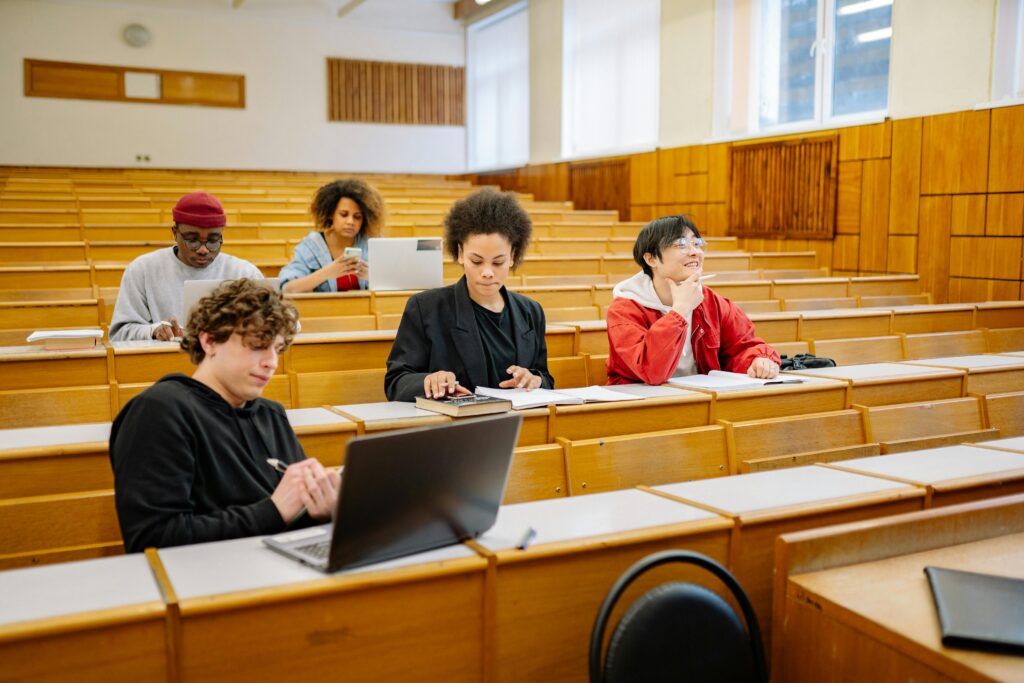 Group of college students studying together in a classroom, focused on learning with laptops and books.